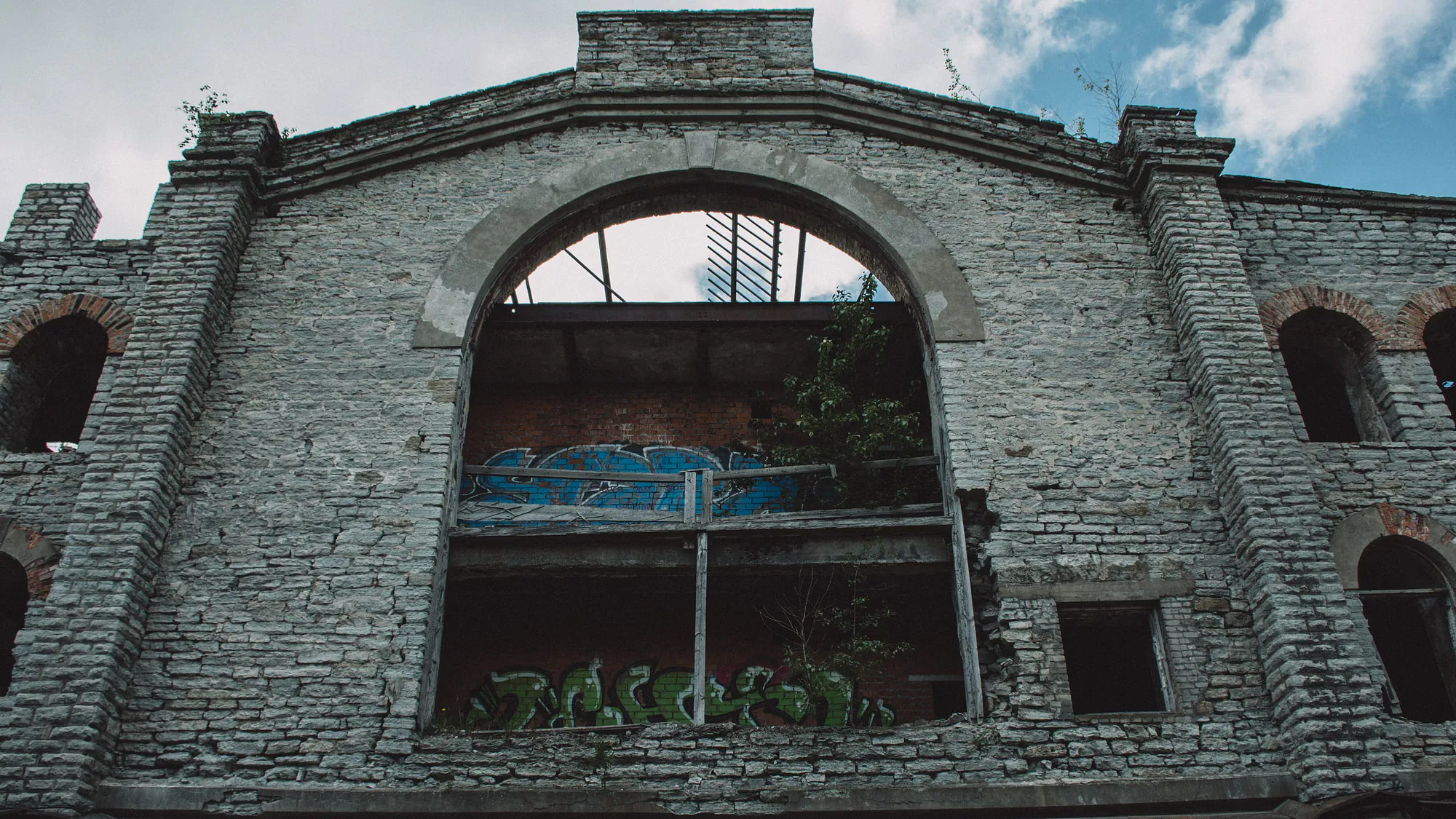 Tall arched opening in the roofless brick shell of an industrial building in Kopli