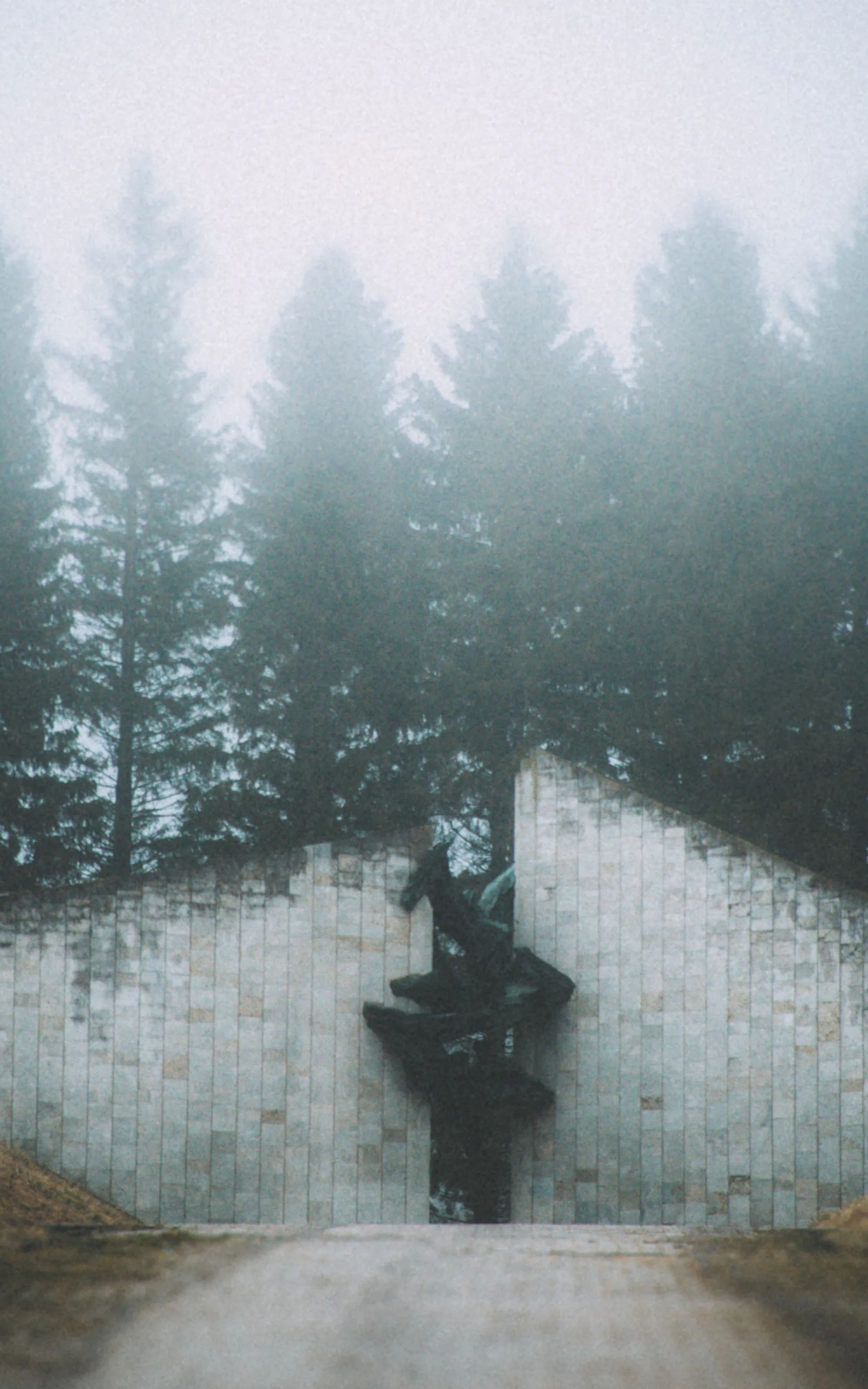Central sculpture framed by angular pale walls and fog-softened conifers at the Estonian Victims of Communism Memorial in Maarjamäe, Tallinn