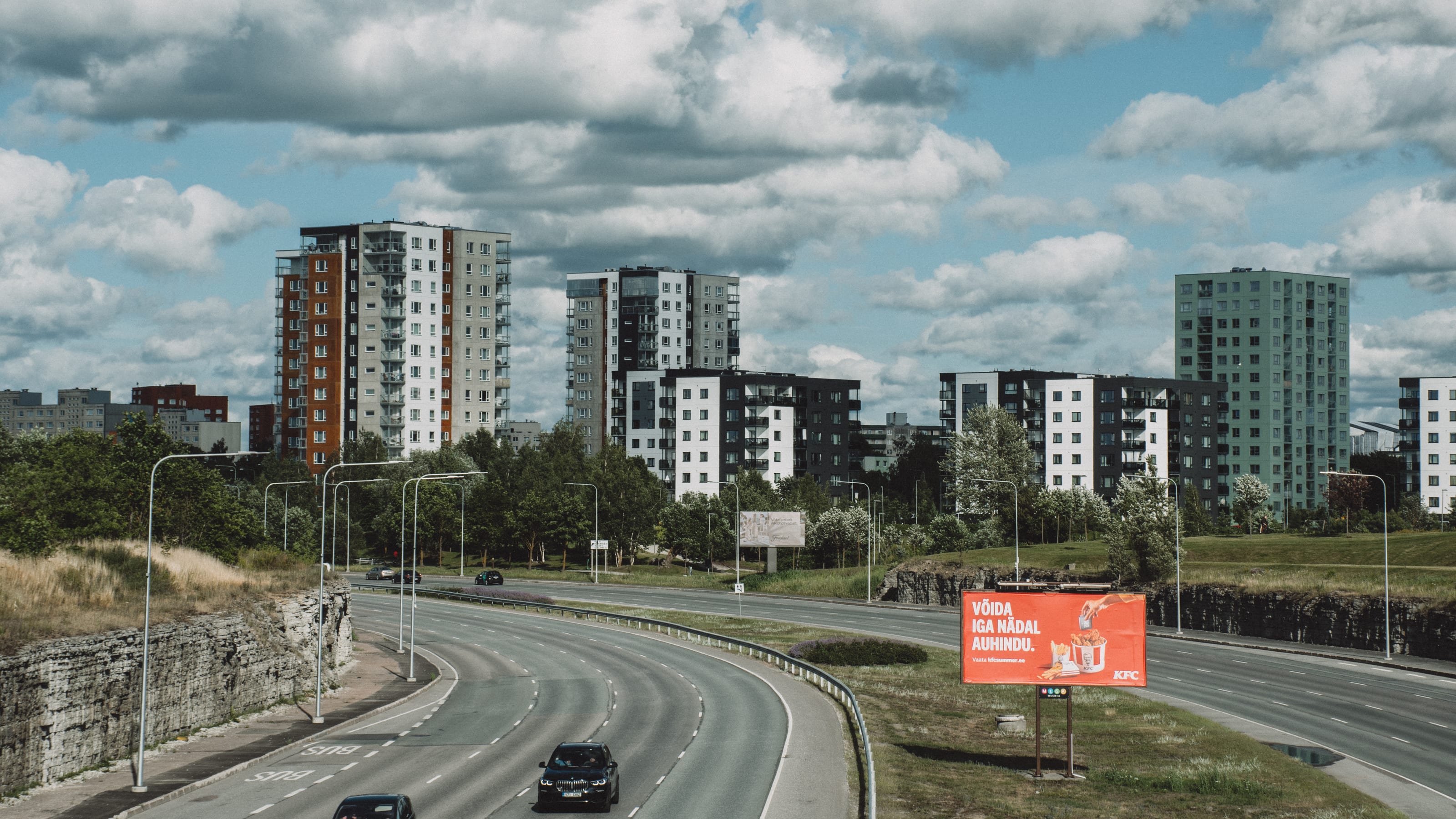 Curving city road beneath apartment towers and summer clouds in Kadriorg Park, Tallinn, Estonia.