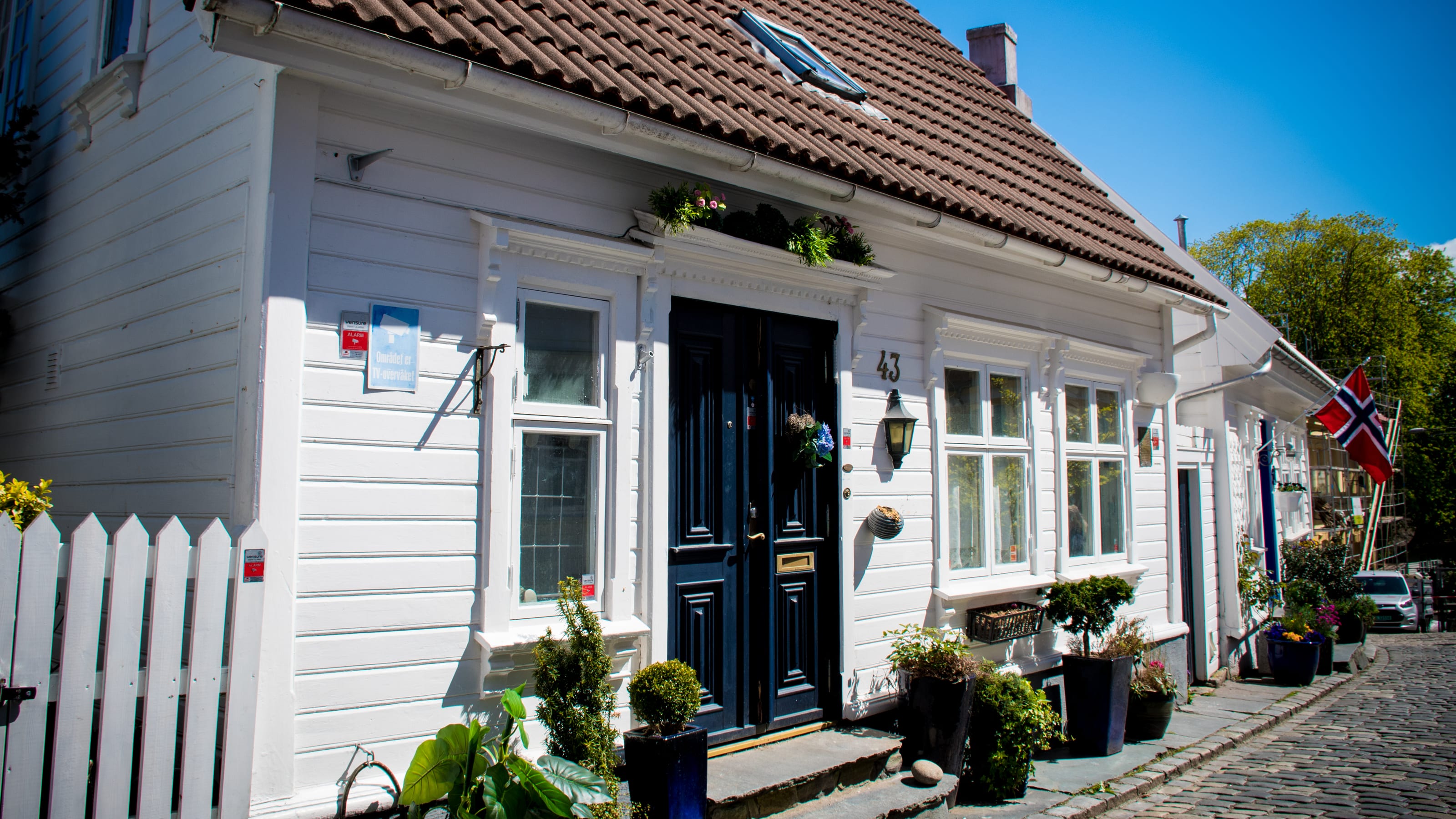 White timber house with a black doorway and flower pots in coastal Norway.