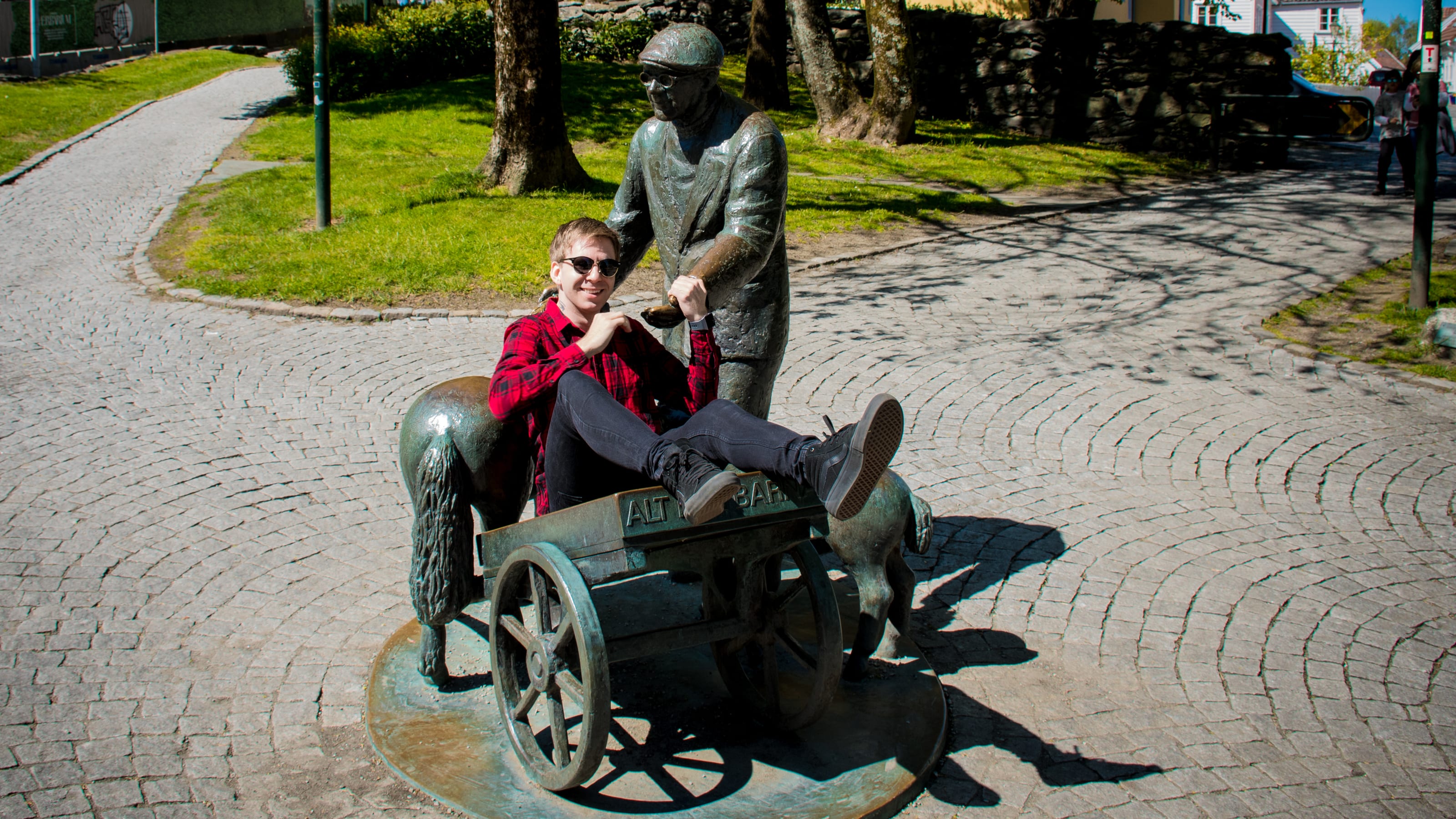 Traveller seated beside a bronze cart sculpture in coastal Norway.