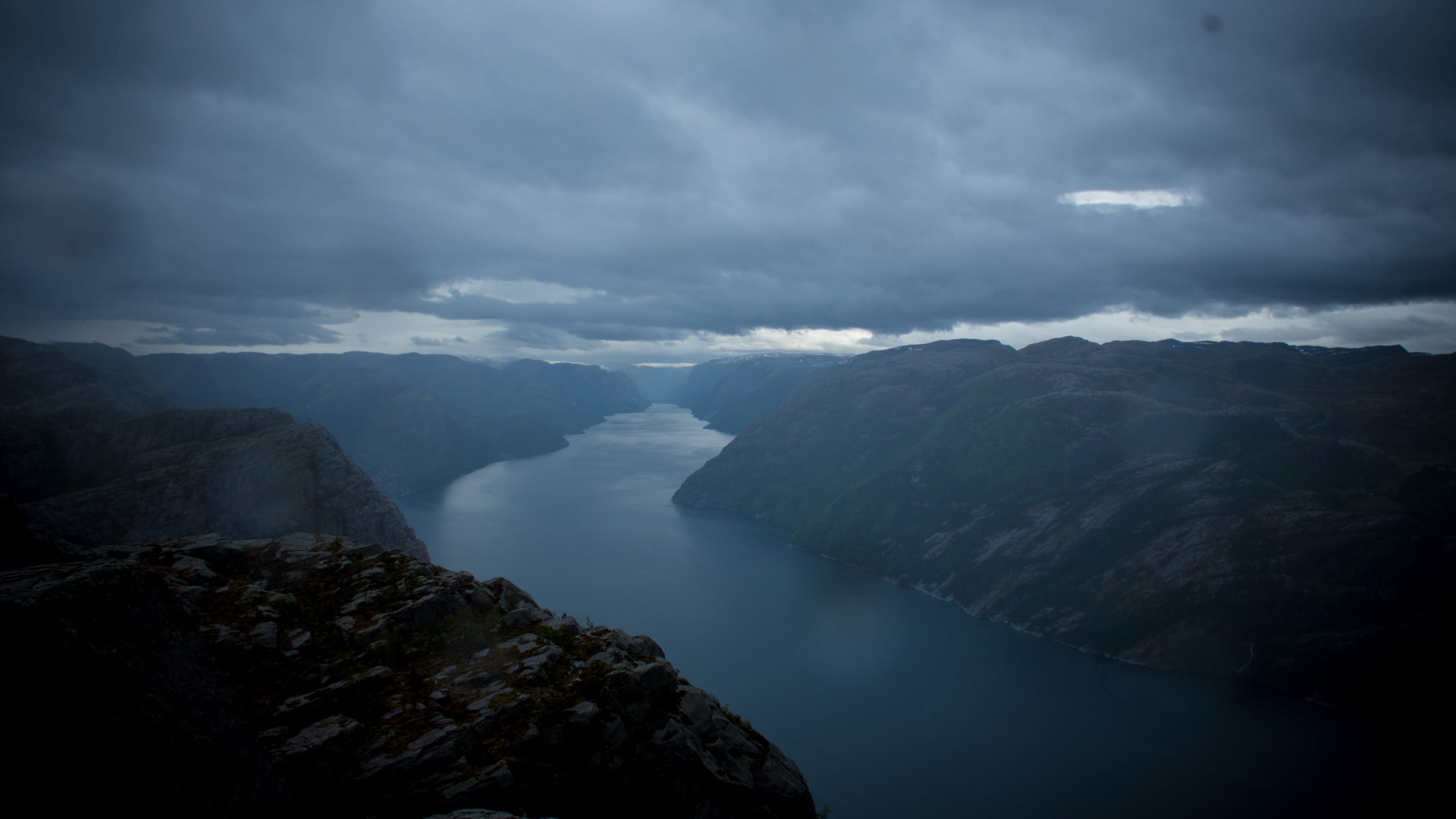 Dark fjord winding between mountains beneath storm clouds in coastal Norway.