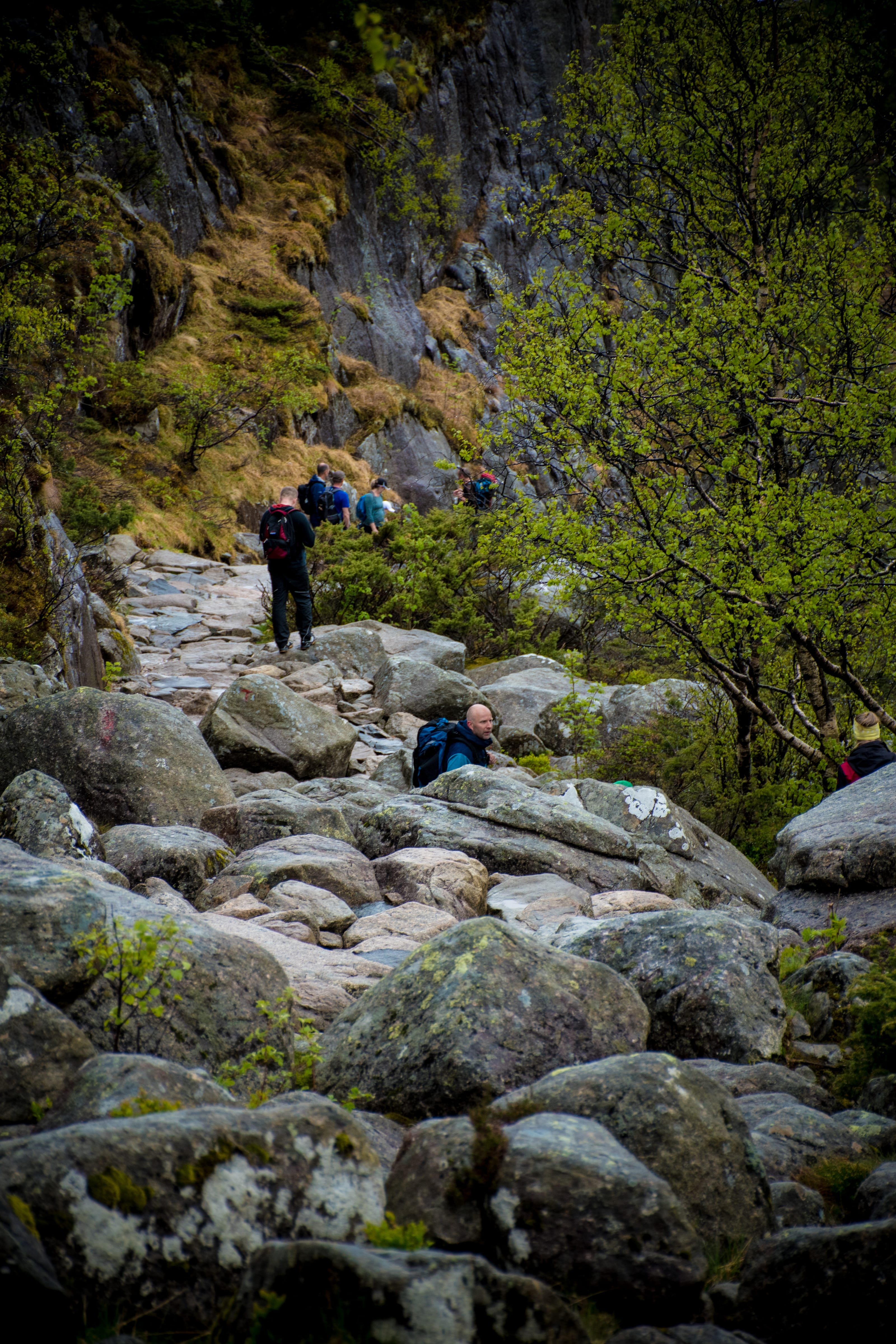 Hiker crossing a boulder-filled mountain trail in coastal Norway.