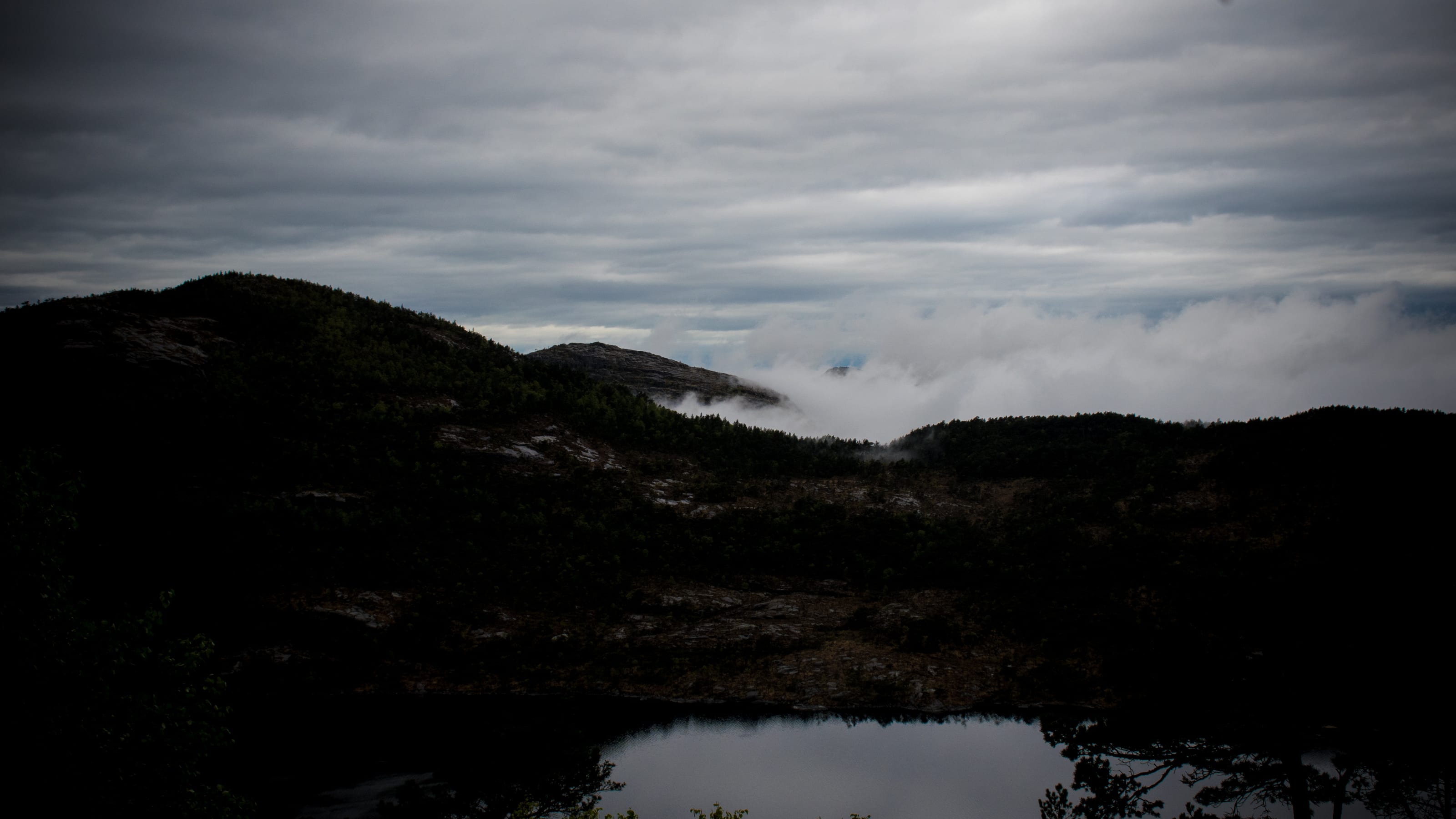 Still mountain tarn beneath a heavy grey sky in coastal Norway.