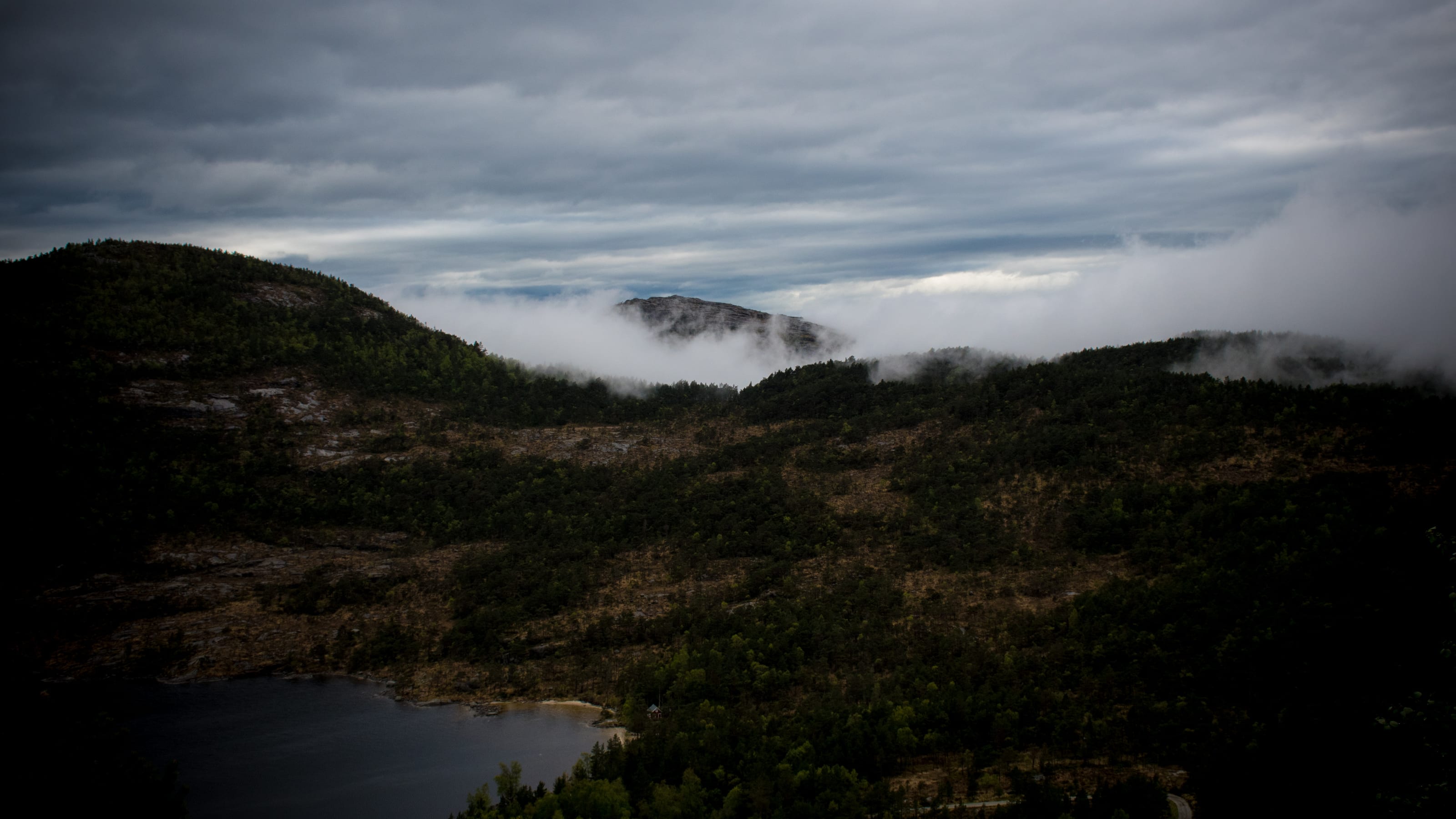 Mist drifting across a mountain lake and dark ridges in coastal Norway.