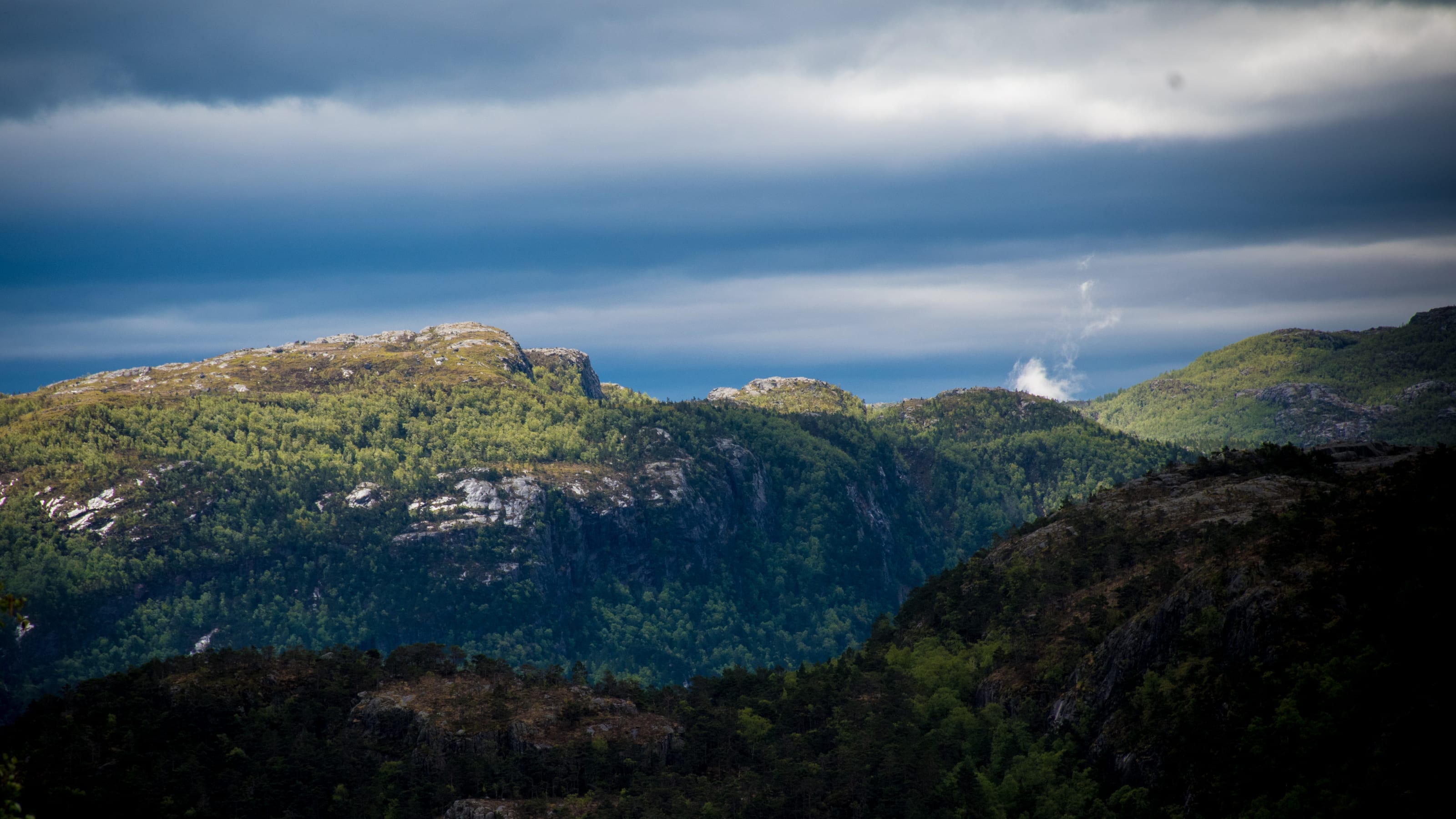 Sunlit mountain shoulder beneath bands of rain cloud in coastal Norway.