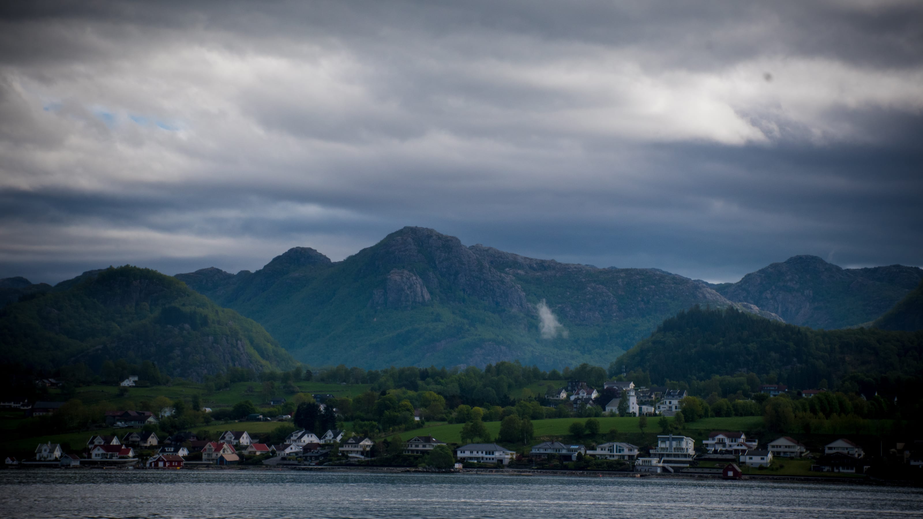 White village and green fields at the foot of mountains in coastal Norway.