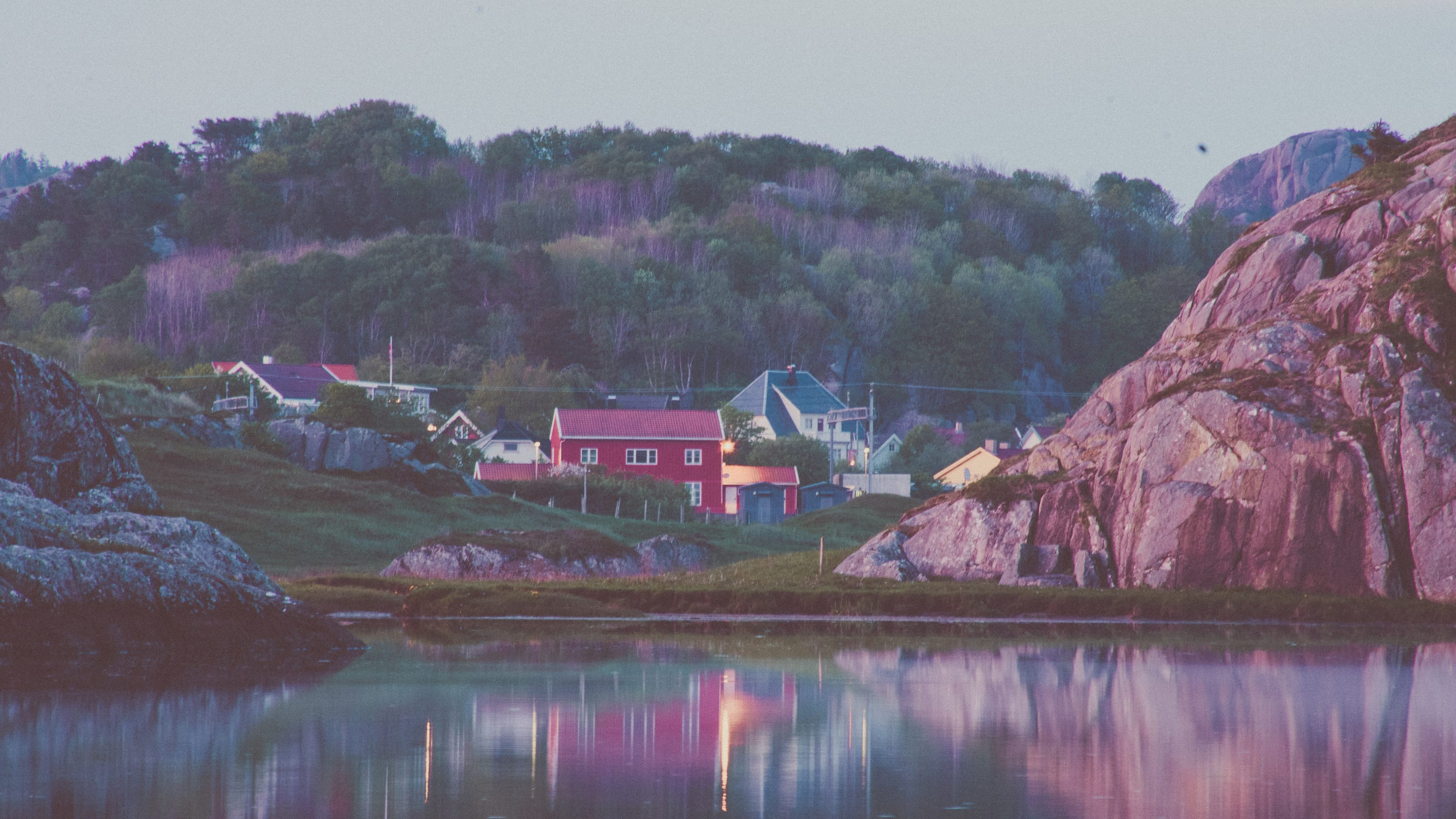Red cabin and granite shore in blue evening light in coastal Norway.