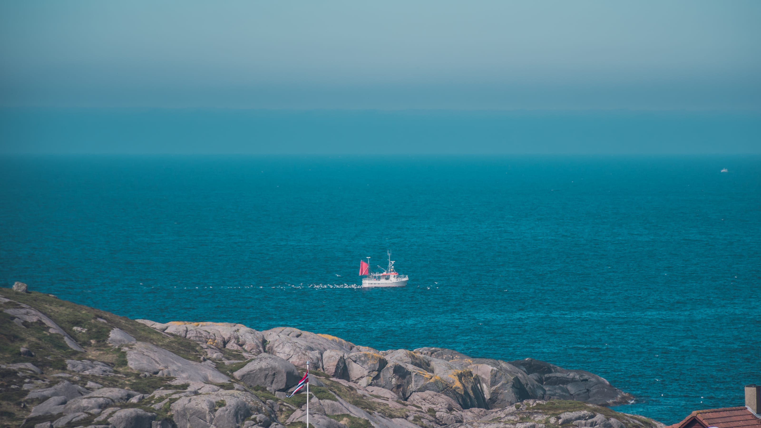 Small vessel crossing the open sea beyond a granite shoreline in coastal Norway.
