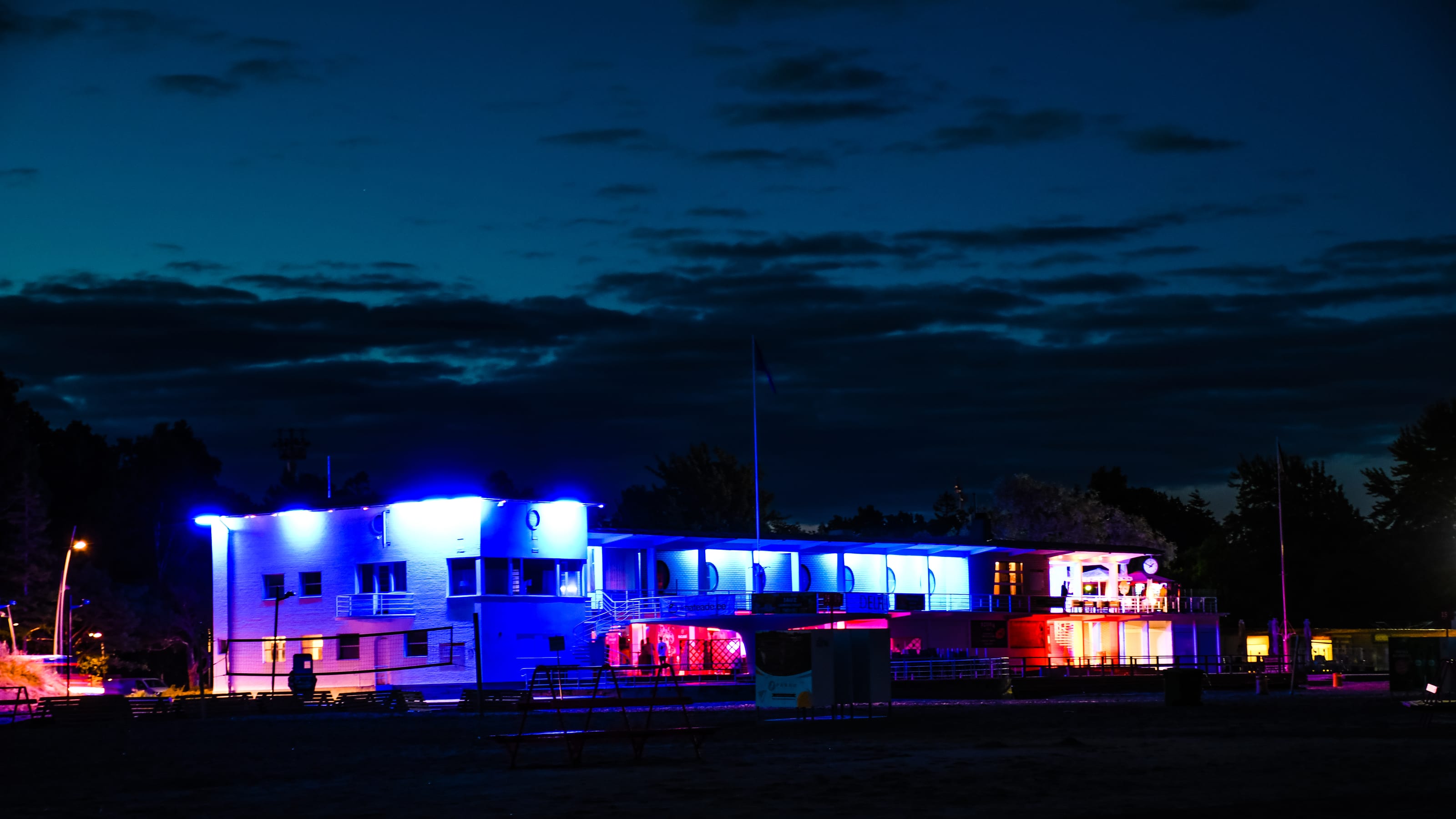 Illuminated roadside building beneath a deep blue night sky in Tolkuse Bog, Estonia.
